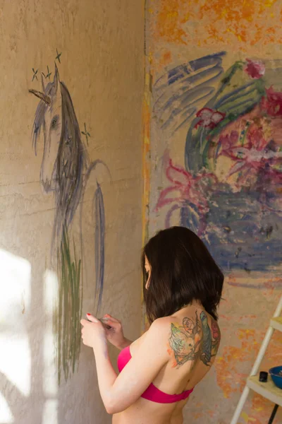 Beautiful girl artist paints on the wall of the unicorn — Stock Photo, Image