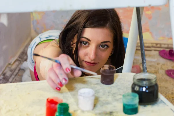 Beautiful girl artist reaching for paints — Stock Photo, Image