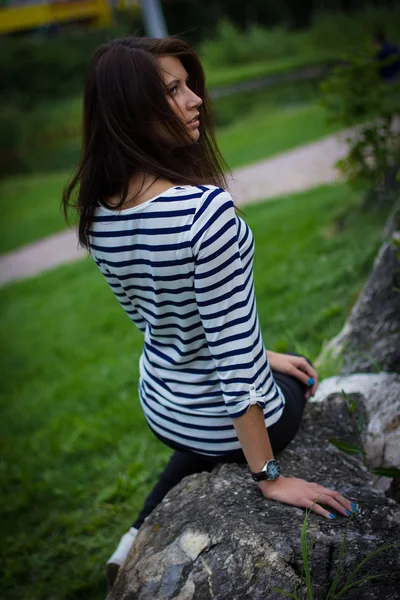 Дівчина в футболці сидить на скелі — стокове фото