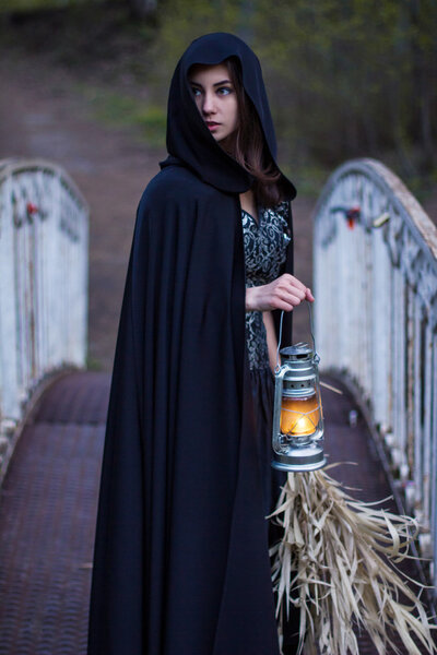 Girl in a black cloak with a lantern on the bridge