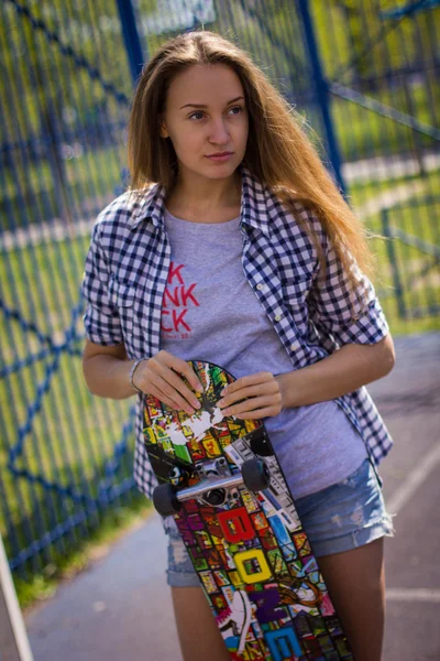 Menina bonito em shorts com um skate no parque infantil — Fotografia de Stock