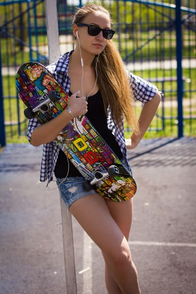 Menina bonito em shorts com um skate no parque infantil — Fotografia de Stock