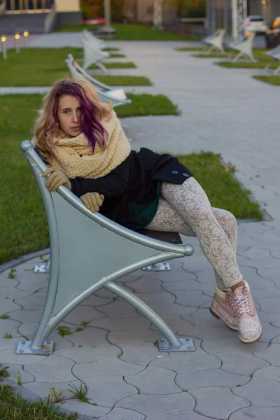 Девушка в пальто сидит на скамейке — стоковое фото