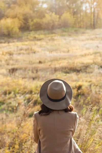 Chica con abrigo y sombrero sentado y mirando a la distancia —  Fotos de Stock