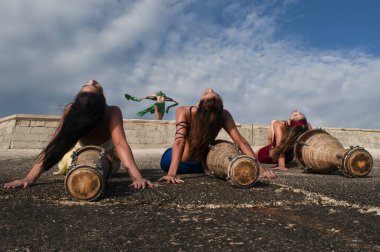 Four girls dressed in different colors with their faces painted posing with drums sitting on their backs on a rocky hill clipart