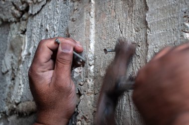 Çekiçle duvara çivi çakıyor. Bitmemiş bir duvar.