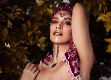 Yüzü Afrika ya da Amazon 'un yerlisi olarak resmedilmiş bir kız, kafasında bir eşarpla, bitki örtüsünün arasında, güzel bir yerli.