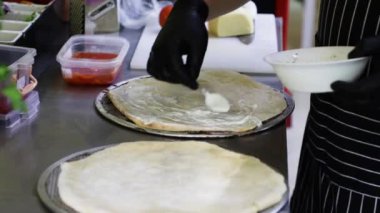 Pizza kabuklarının üzerine metal kaşıkla beyaz sos döküyorum. Mutfakta Yemek Pişirme