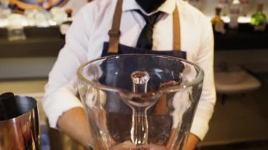 Barmen tezgahta kokteyl hazırlıyor. Cam karıştırıcıda metal maşayla buz yapıyorum. Ellerine siyah eldivenlerle yakın plan çek..
