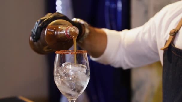 酒保在吧台准备鸡尾酒用瓶子把罗望子汁制成水晶玻璃 里面有冰块 用黑色手套在他手上拍特写 — 图库视频影像