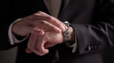 Takım elbiseli genç bir adam kol saati takıyor. Damat elbiseleri
