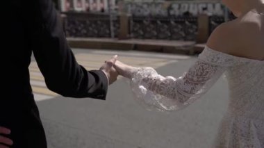 Gelin ve damat el ele tutuşup yaz günü bir şehir caddesinde yürüyorlar. Düğün.