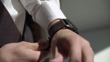 Takım elbiseli genç bir adam kol saati takıyor. Damat elbiseleri