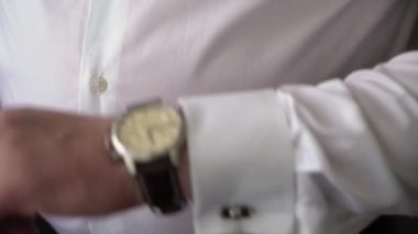 Genç bir adam beyaz bir gömleğe kol düğmesi takıyor. Damat sabahları giyinir.