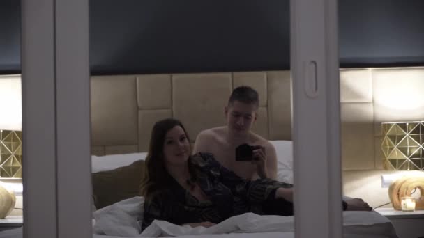 Fiatal szexi pár ölelkezik az ágyban éjszaka — Stock videók