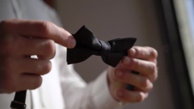 Genç bir adam siyah bir papyon tutuyor. Damat elbiseleri bir etkinlik ya da düğün için ayarlanıyor.