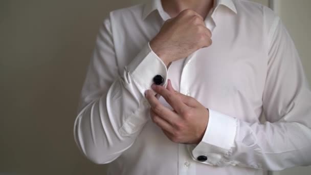 Um jovem coloca abotoaduras em uma camisa branca. O noivo veste-se de manhã — Vídeo de Stock