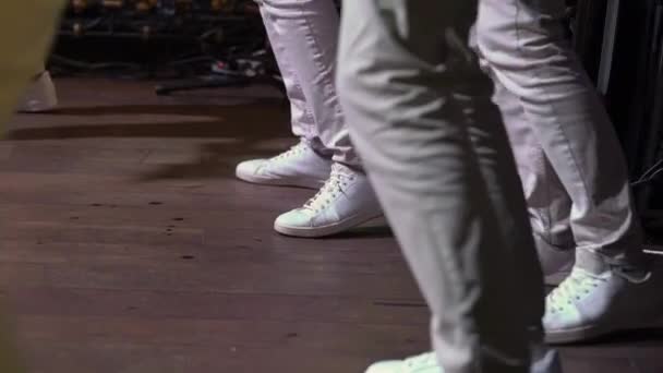 Banda tocando música en concierto, músicos bailando en el escenario, piernas en zapatillas blancas — Vídeo de stock