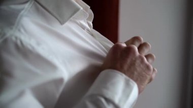 Düğmeleri ilikleyen genç adam beyaz gömlek giydi.