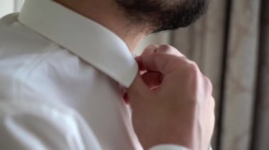 Düğmeleri ilikleyen genç adam beyaz gömlek giydi.