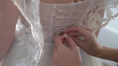 Nedime kravatları ve gelinliğin giyilmesine yardımcı olur. Beyaz elbiseli gelinin sabah hazırlığı.