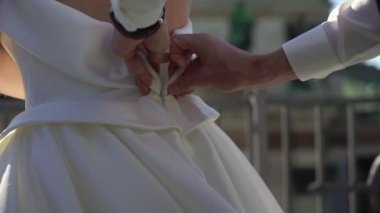 Damat kravatları ve gelinliklerin giyilmesine yardım ediyor. Gelinin beyaz elbisesiyle sabah hazırlığı. Fermuarını çek.