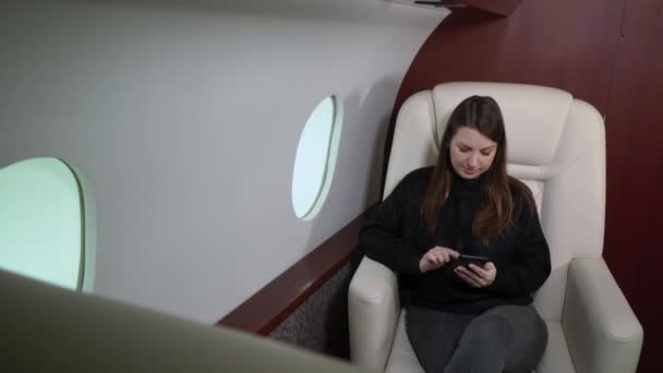 Woman in airplane with mobile phone, using smartphone in first business class or private jet, flight travel — Video