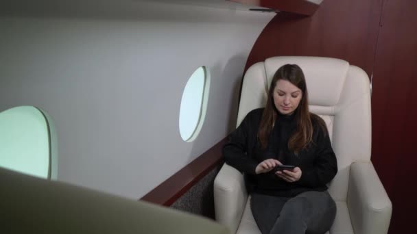 Woman in airplane with mobile phone, using smartphone in first business class or private jet, flight travel — Vídeos de Stock