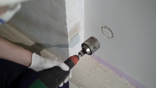 Un trabajador de la construcción que utiliza un perforador hace un agujero en la pared para el electricista, coronando en concreto para el zócalo — Vídeos de Stock