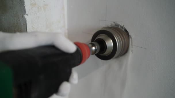 Un trabajador de la construcción que utiliza un perforador hace un agujero en la pared para el electricista, coronando en concreto para el zócalo — Vídeos de Stock