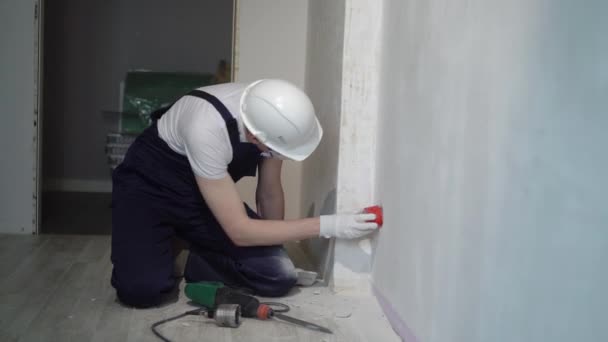 Строитель с помощью бурового штампа проделывает отверстие в стене для электрика, увенчивая бетон для розетки — стоковое видео