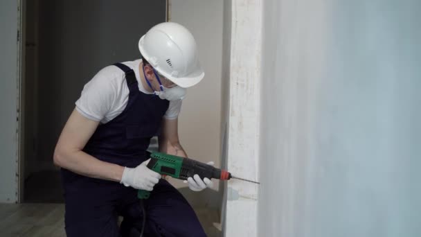 Um construtor de trabalhadores em um canteiro de obras com um soco faz reparos em um apartamento ou uma casa — Vídeo de Stock