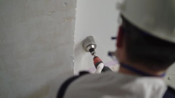 Un trabajador de la construcción que utiliza un perforador hace un agujero en la pared para el electricista, coronando en concreto para el zócalo — Vídeos de Stock