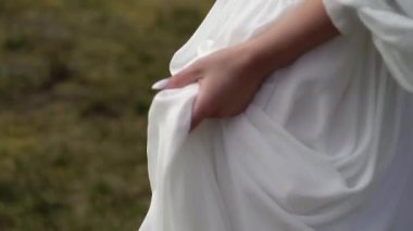 Sarışın gelin tarlada yürüyor, kaldırıyor ve uzun beyaz elbisesini tutuyor..