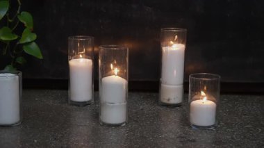 Koyu tencerenin yanında yumuşak bir şekilde parıldayan dört beyaz mum, uzun sütun mumlarının üçlüsü ve temiz kavanozlarda tek bir yemin.