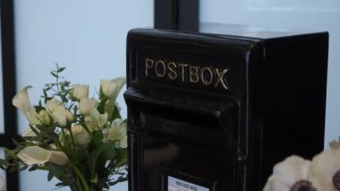 Beyaz Buket 'in yanındaki siyah posta kutusu. Parlak Siyah Metal Posta Kutusunun Kapanışı Etiketli Posta Kutusu Pencerenin kenarında Zarif Beyaz Calla