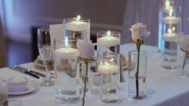 Cam Masa üzerinde yüzen mumlar Serene düğün süsü oluşturur Beyaz güller, kristal cam eşyalar, parlak çatal bıçaklar ve yumuşak mavi