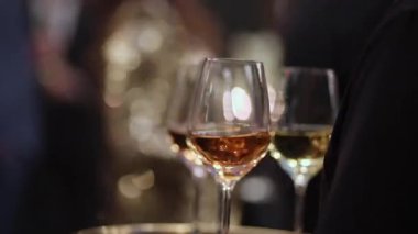 Bulanık misafirler ve arka planda sıcak Bokeh ışıkları ve sakin bir akşam resepsiyonunda üç tane gül şarabı kadehi.