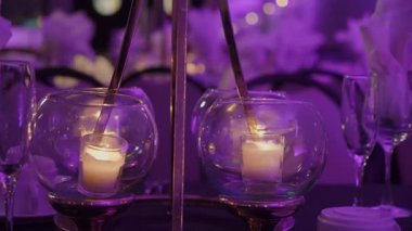 Şölen masasında cam kaselerde parlayan adak mumları, Mor Işık Altında İnce Tunes Düzenlemesi, Yanıp sönen Alevler Yansıması
