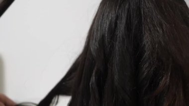 Saç stilisti, uzun kıvırcık, saç maşalı, elleri kıvırcık, elleri kapalı, salon aletleri görünür, odaklanmış teknikleri var.