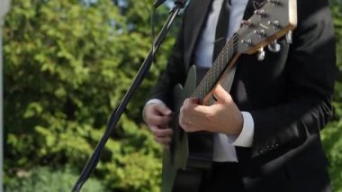 Siyah Takım Elbiseli Erkek Gitarist, Mikrofon Yanında Akustik Gitar Çalıyor, Elleri Kapalı ve Parmakları Çalan Akortlar ve Teller,