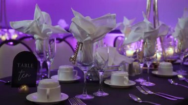 Katlanmış peçeteler, siyah örtüler, cilalı çatal bıçak takımı ve kristal cam eşyalar, beyaz çiçeklerle süslenmiş uzun masa örtüleri.,