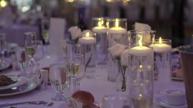 Mum ışığında akşam yemeği için hazırlanan masa örtüsü, uzun silindirlerde yüzen mumlar, köpüklü şampanya flütleri ve su bardakları,