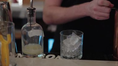 Beyaz barmen bardağa kokteyl dolduruyor. Titretici ve süzgeç kullanılıyor. Citrus Bitters Jigger ile ölçüldü.