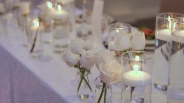 Solgun güller ve yüzen mumlar, su ve gövdeli küçük cam vazolar, sıcak alevli uzun silindir konuşmalar, beyaz keten masa.