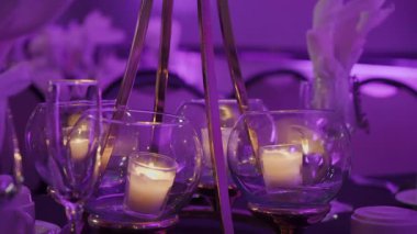 Şölen masasında cam kaselerde parlayan adak mumları, Mor Işık Altında İnce Tunes Düzenlemesi, Yanıp sönen Alevler Yansıması