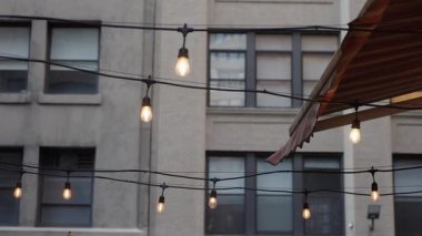 Çatı İp Işıkları Pencerelerin Üzerinde, Tuvalin Altında Yumuşak Sıcak Ampuller, Şehir Beton Cephesi, Hafif Karanlık Parıltısı, Konforlu Bistro