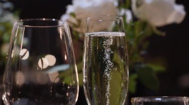 Arka planda yükselen baloncuklu şampanya flütü ve gül buketi, sıcak Bokeh ışıkları ve zarif masa süsü, kutlama atmosferi.