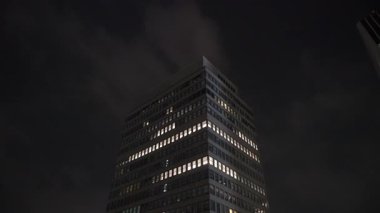 Düşük Açı Ofis Kulesi Bulutların Altında Yinelenen Aydınlatma Pencereleri ve Düşünceli Gece Gökyüzüne Karşı Yüksek Çerçeveli Cam Yüzle,