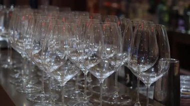 Bar tezgahı boyunca sıralanmış boş şarap kadehleri, ışıldayan kristal yansımaları, yumuşak Bokeh arka planı, restoran ambiyansı, resepsiyon